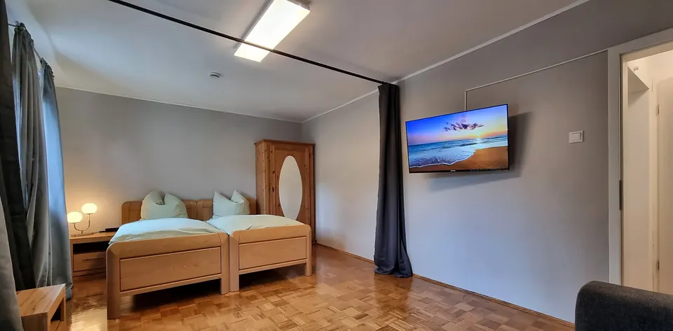 Helles Zimmer mit Doppelbett aus Holz, Kleiderschrank und Flachbild-TV