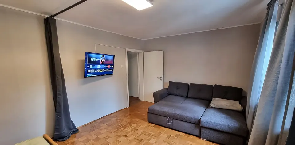 Graues Ecksofa auf Parkett, Fernseher an der Wand