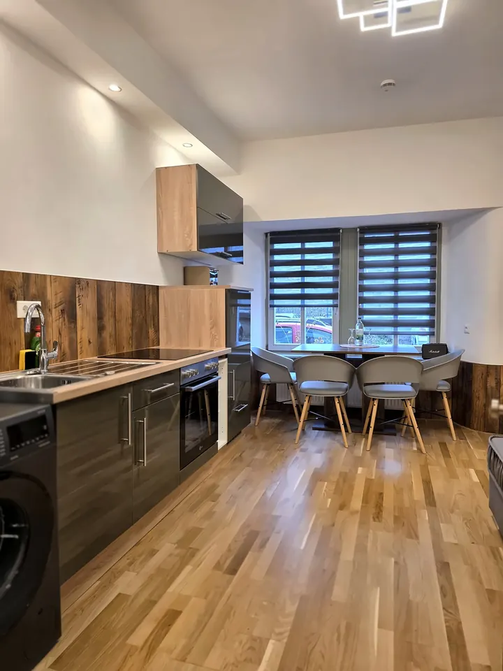 Wohnküche mit dunklen Fronten, Holzrückwand und Esstisch